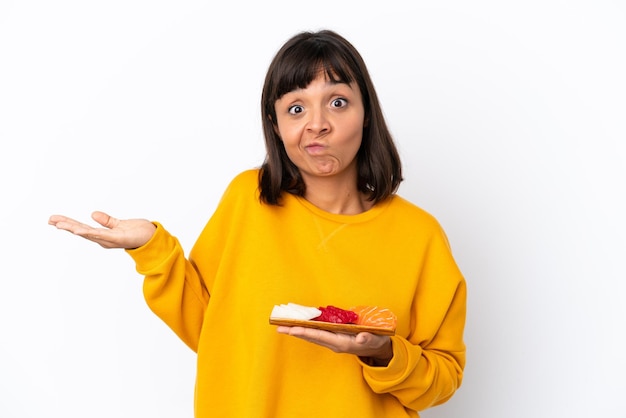Young mixed race woman holding sashimi isolated on white background having doubts while raising hands