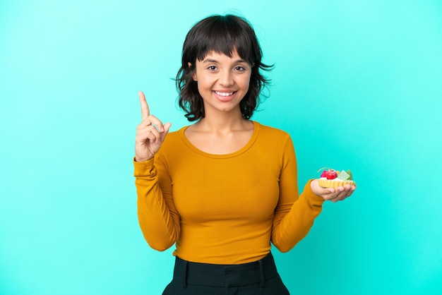 素晴らしいアイデアを指している青い背景で隔離のタルトを保持している若い混血の女性