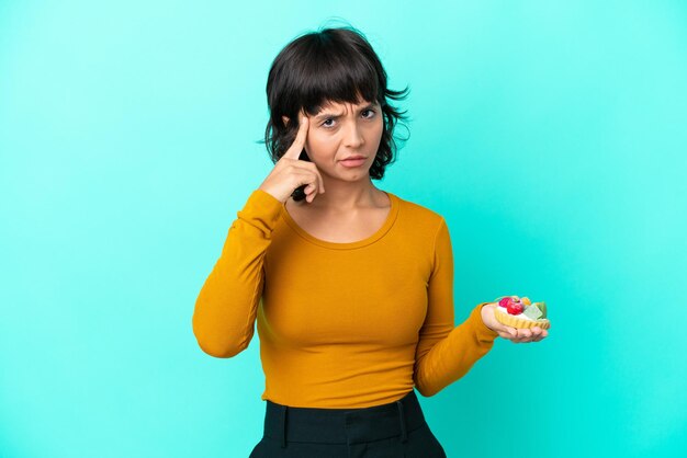 Young mixed race woman holding a tartlet isolated on blue background thinking an idea