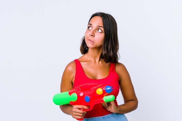 Young mixed race woman holding a water gun isolated confused, feels doubtful and unsure.