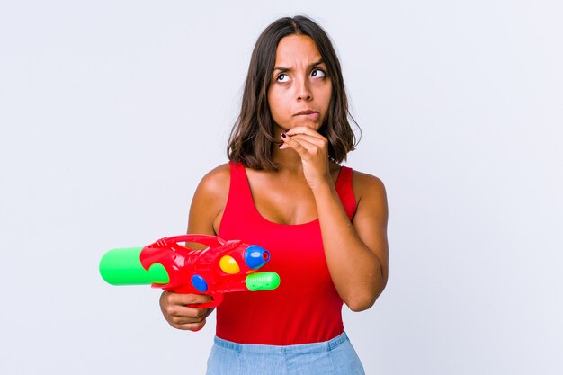 Young mixed race woman holding a water gun isolated contemplating, planning a strategy, thinking about the way of a business.