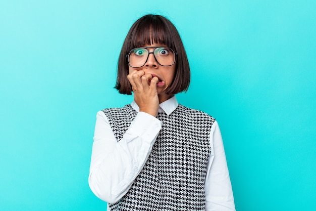 Young mixed race woman isolated on blue background biting fingernails, nervous and very anxious.