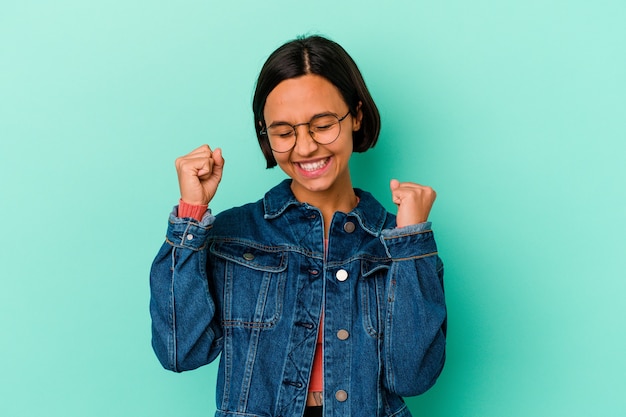 Young mixed race woman isolated on blue background celebrating a special day, jumps and raise arms with energy.