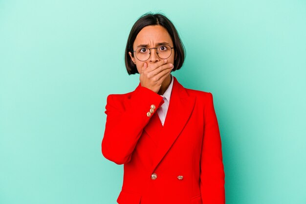 Young mixed race woman isolated on blue background covering mouth with hands looking worried.