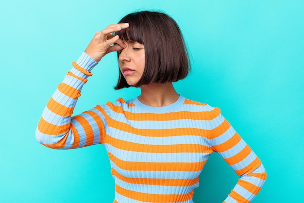 Young mixed race woman isolated on blue background having a head ache, touching front of the face.