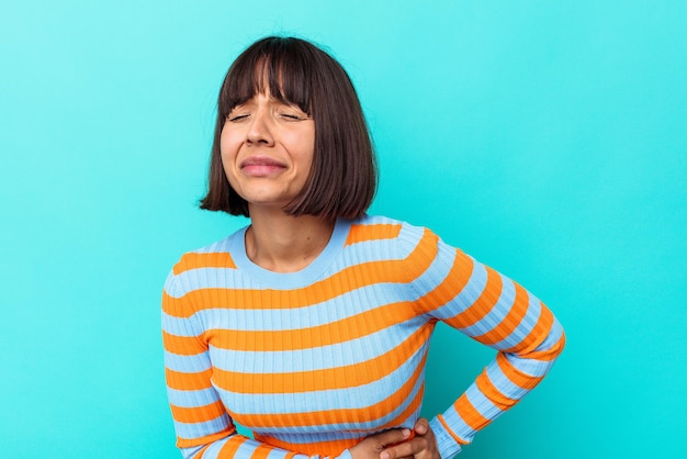 Young mixed race woman isolated on blue background having a liver pain, stomach ache.