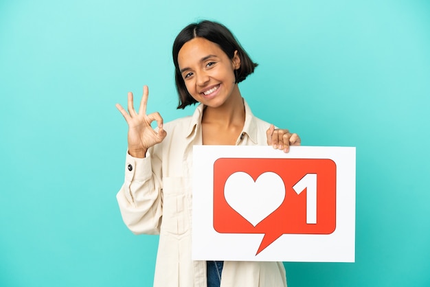 Young mixed race woman isolated on blue background holding a placard with Like icon and celebrating a victory