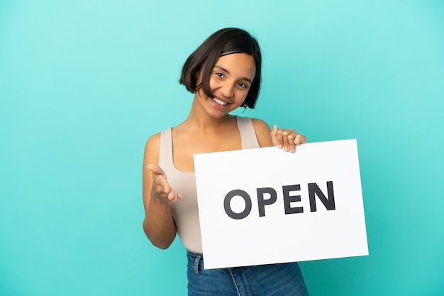 Young mixed race woman isolated on blue background holding a placard with text OPEN making a deal