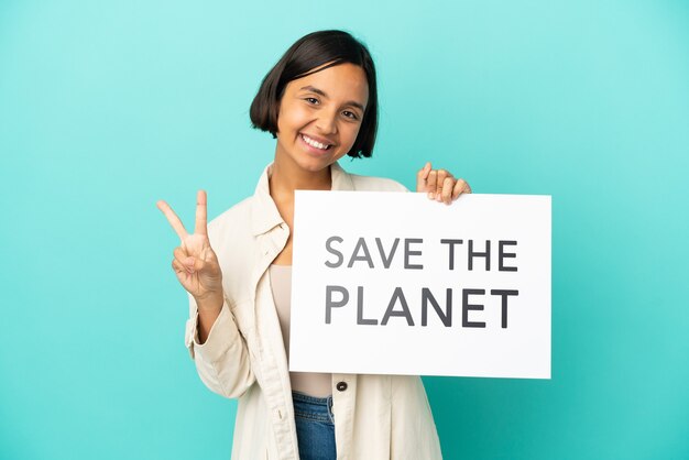 young mixed race woman isolated on blue background holding a placard with text save the planet and celebrating a victory