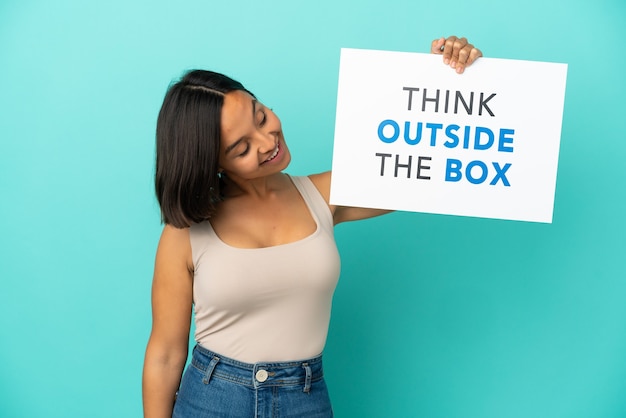 Young mixed race woman isolated on blue background holding a placard with text Think Outside The Box