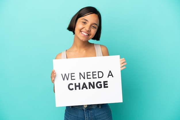 Young mixed race woman isolated on blue background holding a placard with text We Need a Change with happy expression