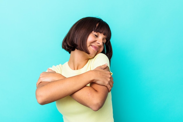 Young mixed race woman isolated on blue background hugs, smiling carefree and happy.