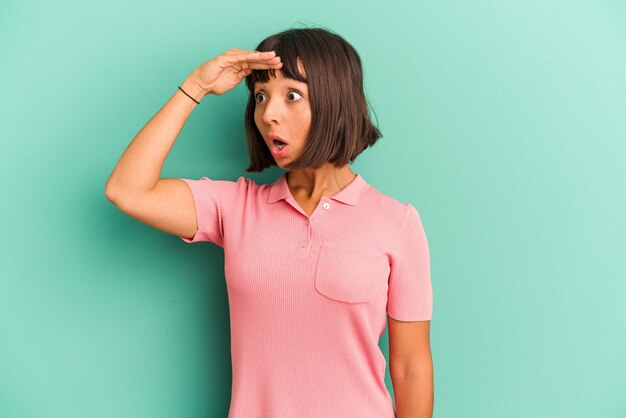 Young mixed race woman isolated on blue background looking far away keeping hand on forehead.