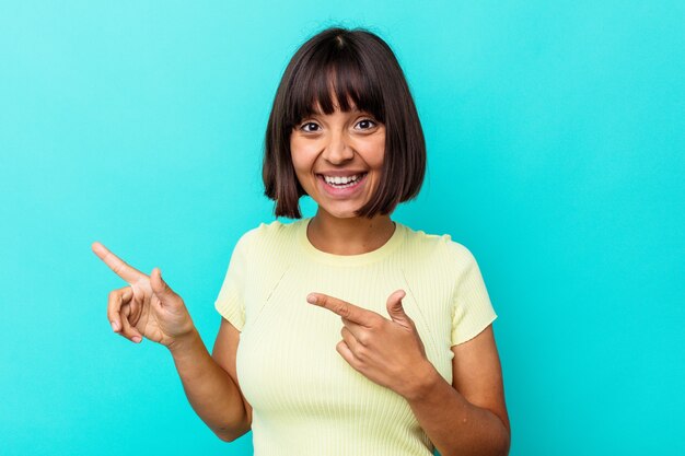 Young mixed race woman isolated on blue background pointing with forefingers to a copy space, expressing excitement and desire.