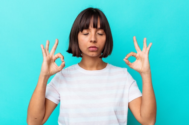 Young mixed race woman isolated on blue background relaxes after hard working day, she is performing yoga.