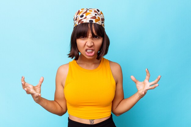 Young mixed race woman isolated on blue background screaming with rage.