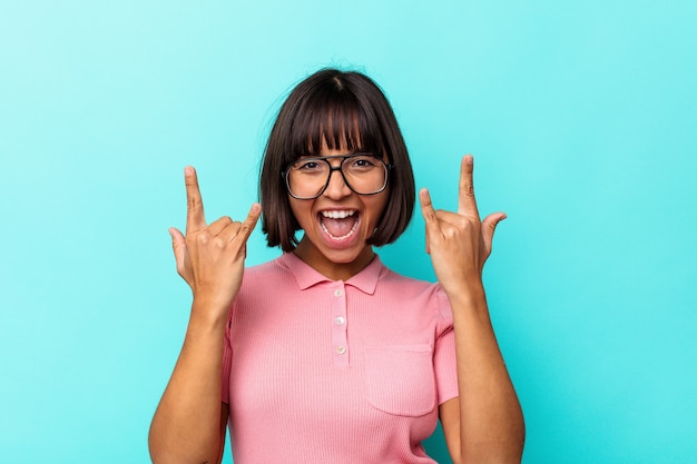 Photo young mixed race woman isolated on blue background showing a horns gesture as a revolution concept.