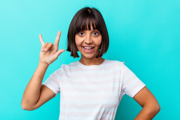 革命の概念として角のジェスチャーを示す青い背景に分離された若い混血の女性。