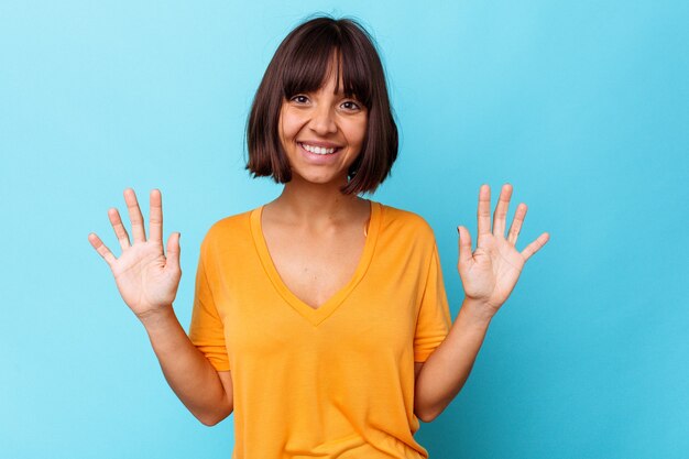 Молодая женщина смешанной расы, изолированные на синем фоне, показывая номер десять руками.