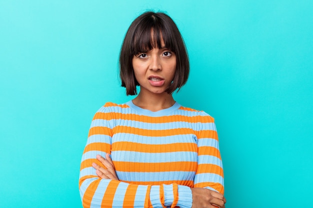 Young mixed race woman isolated on blue background suspicious, uncertain, examining you.