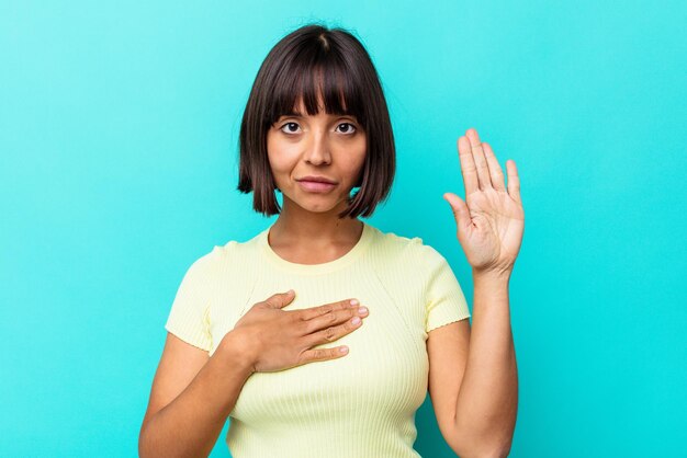 Young mixed race woman isolated on blue background taking an oath, putting hand on chest.