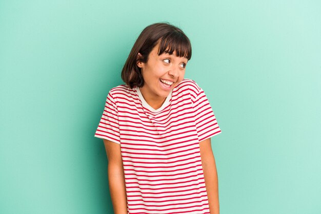 Young mixed race woman isolated on blue background winks an eye and holds an okay gesture with hand.