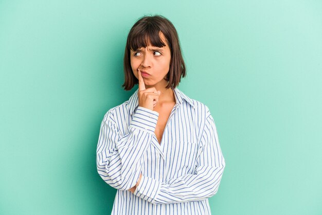 Young mixed race woman isolated on blue looking sideways with doubtful and skeptical expression.