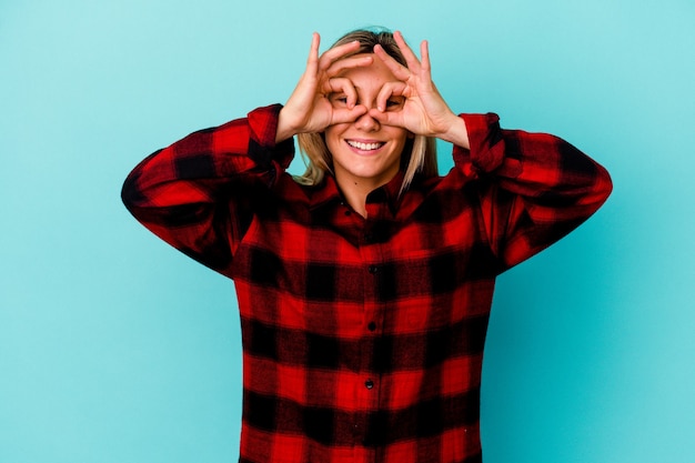 Young mixed race woman isolated on blue wall excited keeping ok gesture on eye.