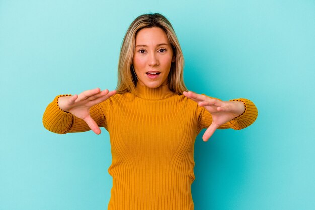 Young mixed race woman isolated on blue wall holding something with palms, offering to camera.