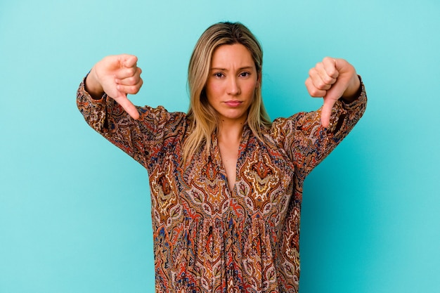 Young mixed race woman isolated on blue wall showing a dislike gesture, thumbs down. Disagreement concept.