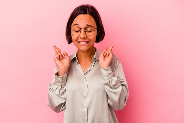 Young mixed race woman isolated on pink background crossing fingers for having luck