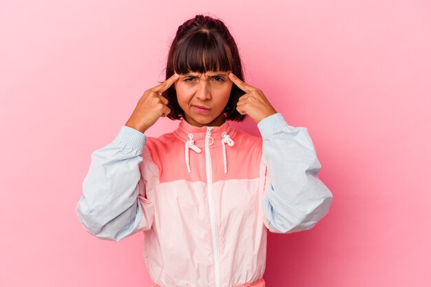 Young mixed race woman isolated on pink background focused on a task, keeping forefingers pointing head.