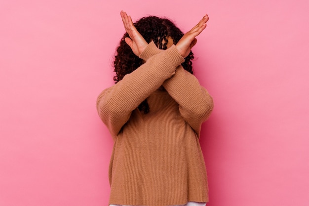 Foto giovane donna di razza mista isolata su sfondo rosa mantenendo due braccia incrociate, concetto di negazione.