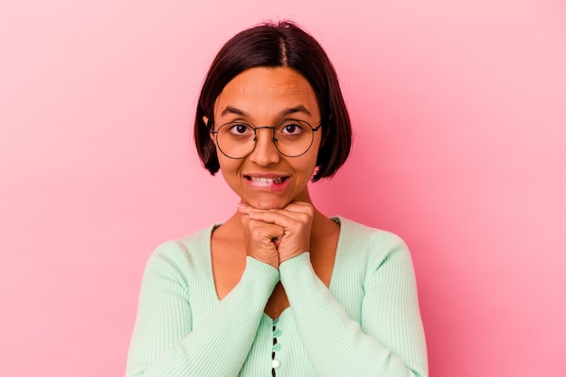 Young mixed race woman isolated on pink background keeps hands under chin, is looking happily aside.