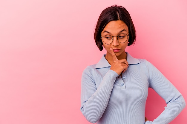 Young mixed race woman isolated on pink background looking sideways with doubtful and skeptical expression.