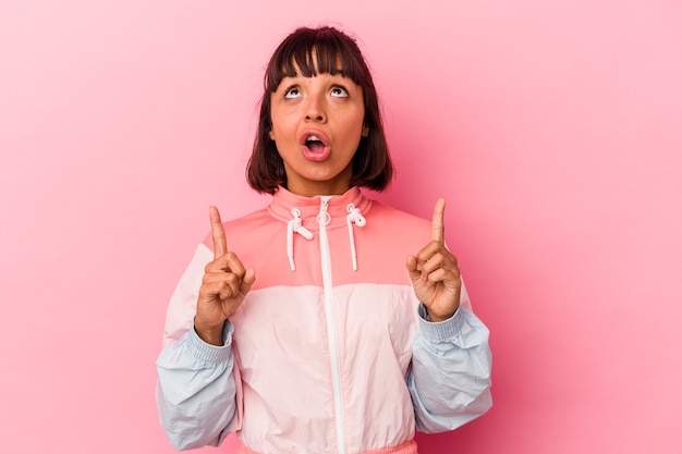 Young mixed race woman isolated on pink background pointing upside with opened mouth.