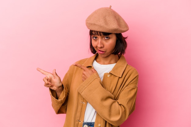 Young mixed race woman isolated on pink background pointing with forefingers to a copy space, expressing excitement and desire.