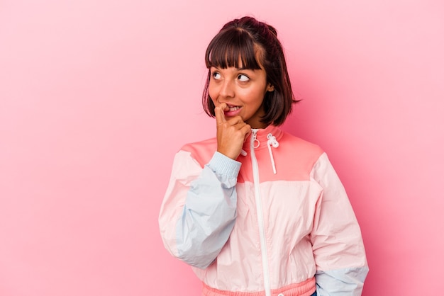 Young mixed race woman isolated on pink background relaxed thinking about something looking at a copy space.