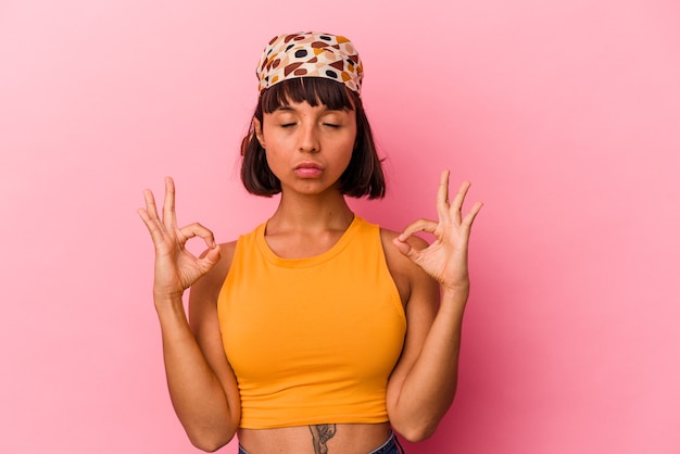 Young mixed race woman isolated on pink background relaxes after hard working day, she is performing yoga.