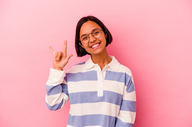 Young mixed race woman isolated on pink background showing a horns gesture as a revolution concept.