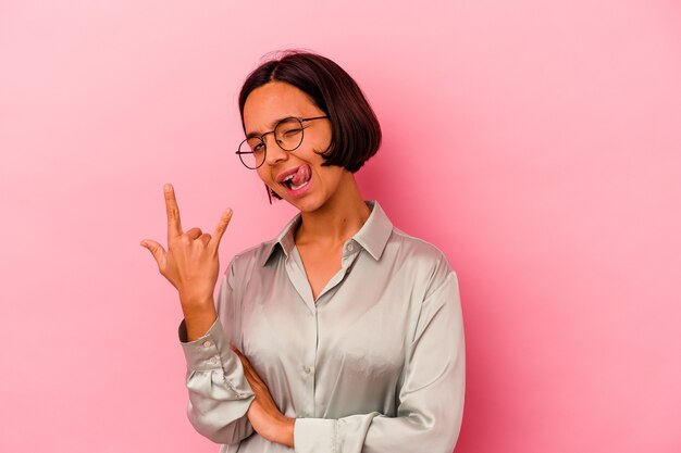 Young mixed race woman isolated on pink background showing rock gesture with fingers