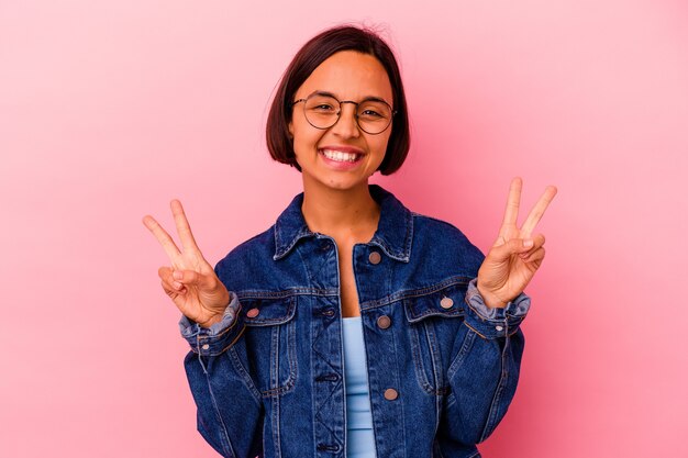 Young mixed race woman isolated on pink background showing victory sign and smiling broadly.