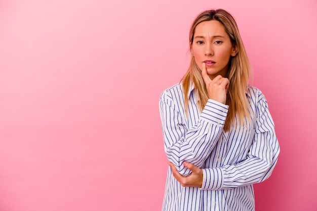 Young mixed race woman isolated on pink looking sideways with doubtful and skeptical expression.