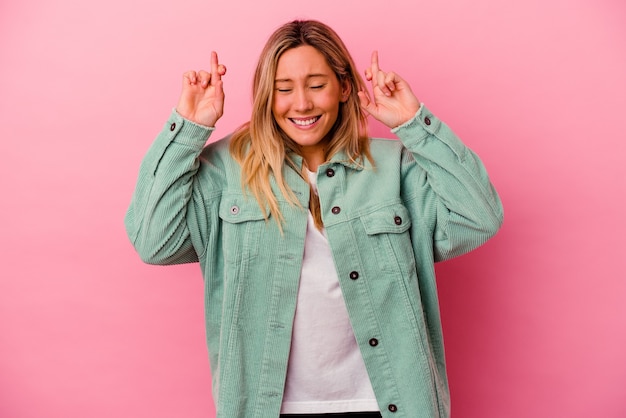 Young mixed race woman isolated on pink wall crossing fingers for having luck