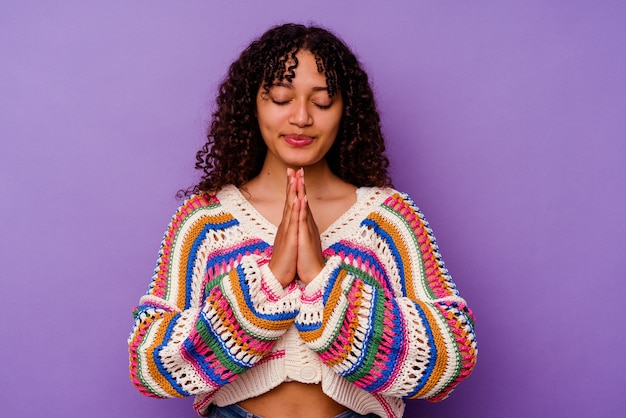 Young mixed race woman isolated on purple background holding hands in pray near mouth, feels confident.