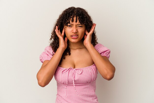 Young mixed race woman isolated on white background covering ears with fingers, stressed and desperate by a loudly ambient.