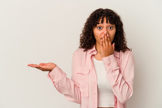 Young mixed race woman isolated on white background impressed holding copy space on palm.