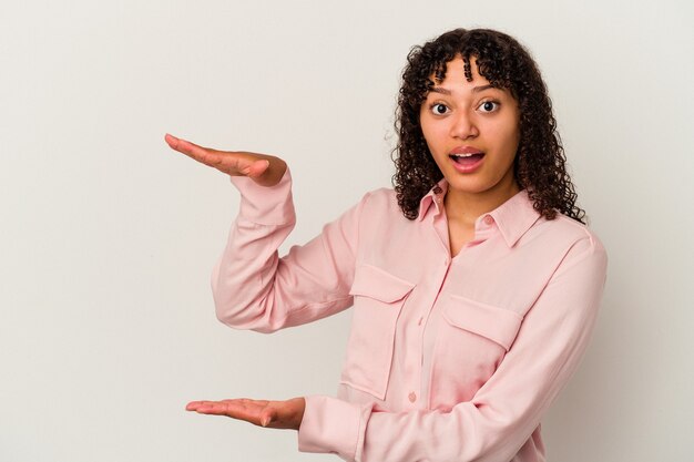 Young mixed race woman isolated on white background shocked and amazed holding a copy space between hands.