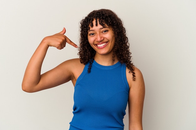 Young mixed race woman isolated on white wall person pointing by hand to a shirt copy space, proud and confident