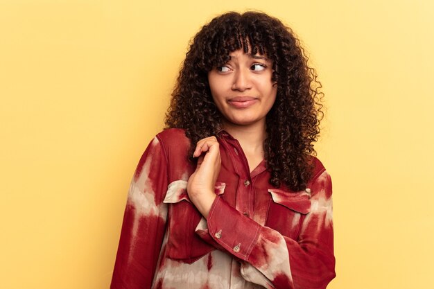 Young mixed race woman isolated on yellow background confused, feels doubtful and unsure.